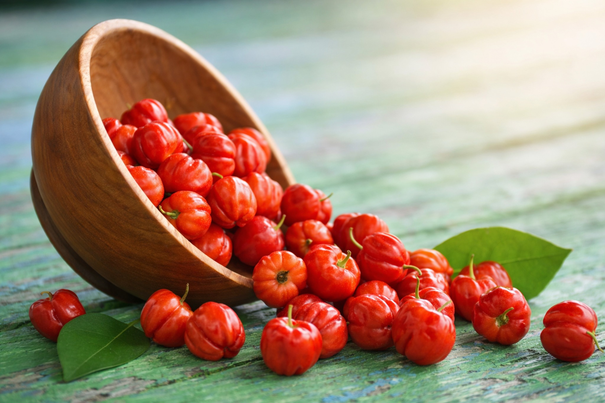 Fresh red acerola cherries spilling from a wooden bowl